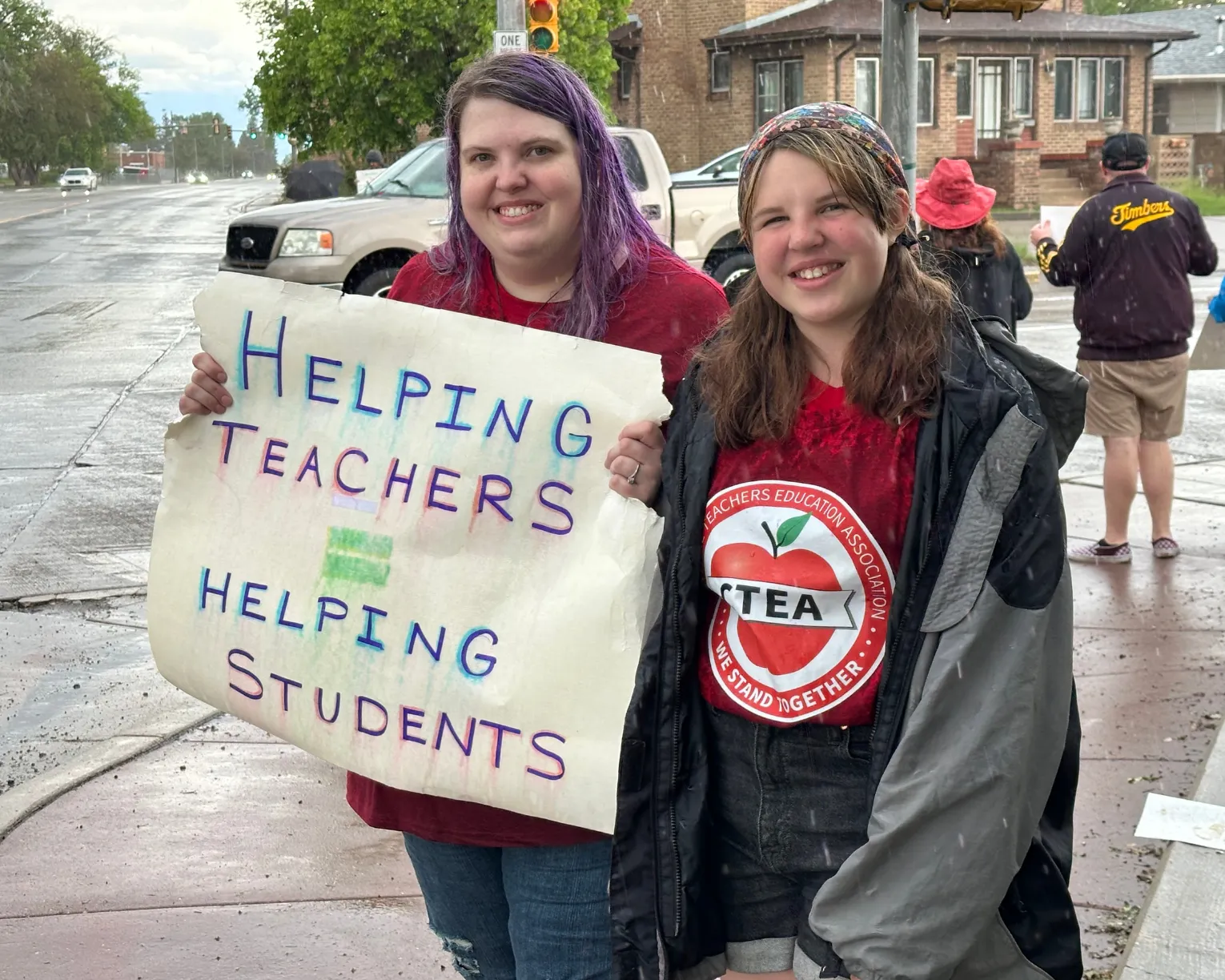 Two members pose for a picture at the Cheyenne rally. One member holds a sign that reads, "Helping Teachers = Helping Students"