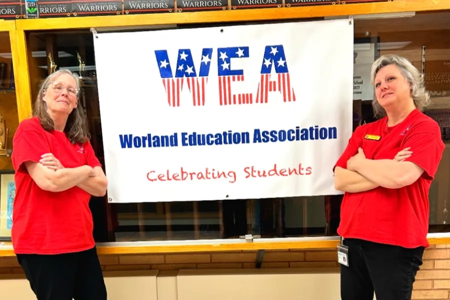 WEA members stand by a banner with arms folded and playful expressions